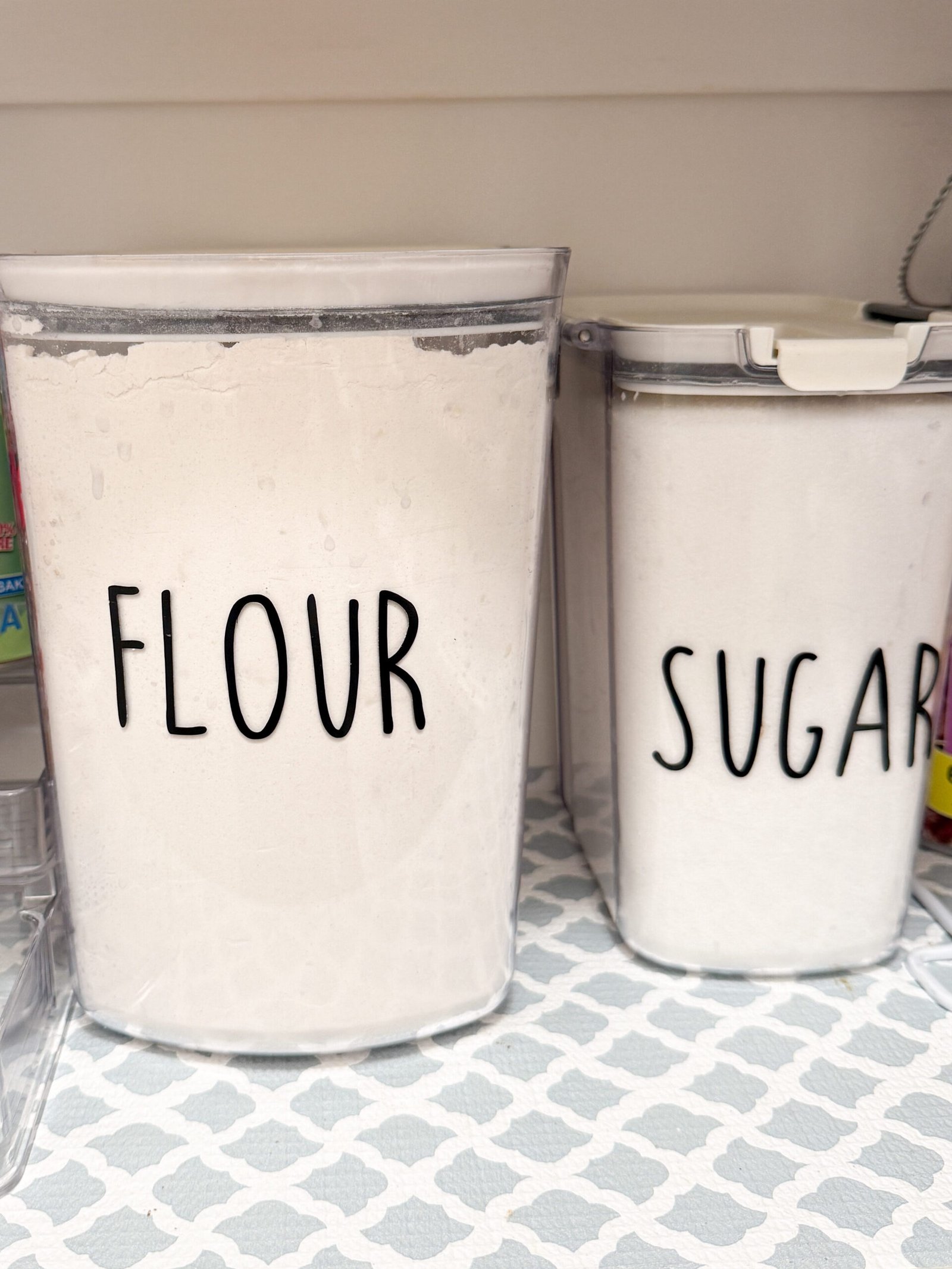 Organized pantry corner featuring labeled flour and labeled sugar containers with neutral pantry shelf liner.