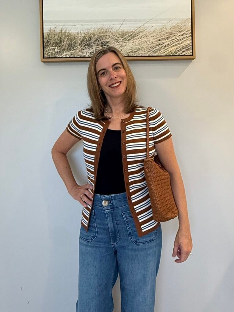Women wearing a open front cardigan with jeans and a woven purse.