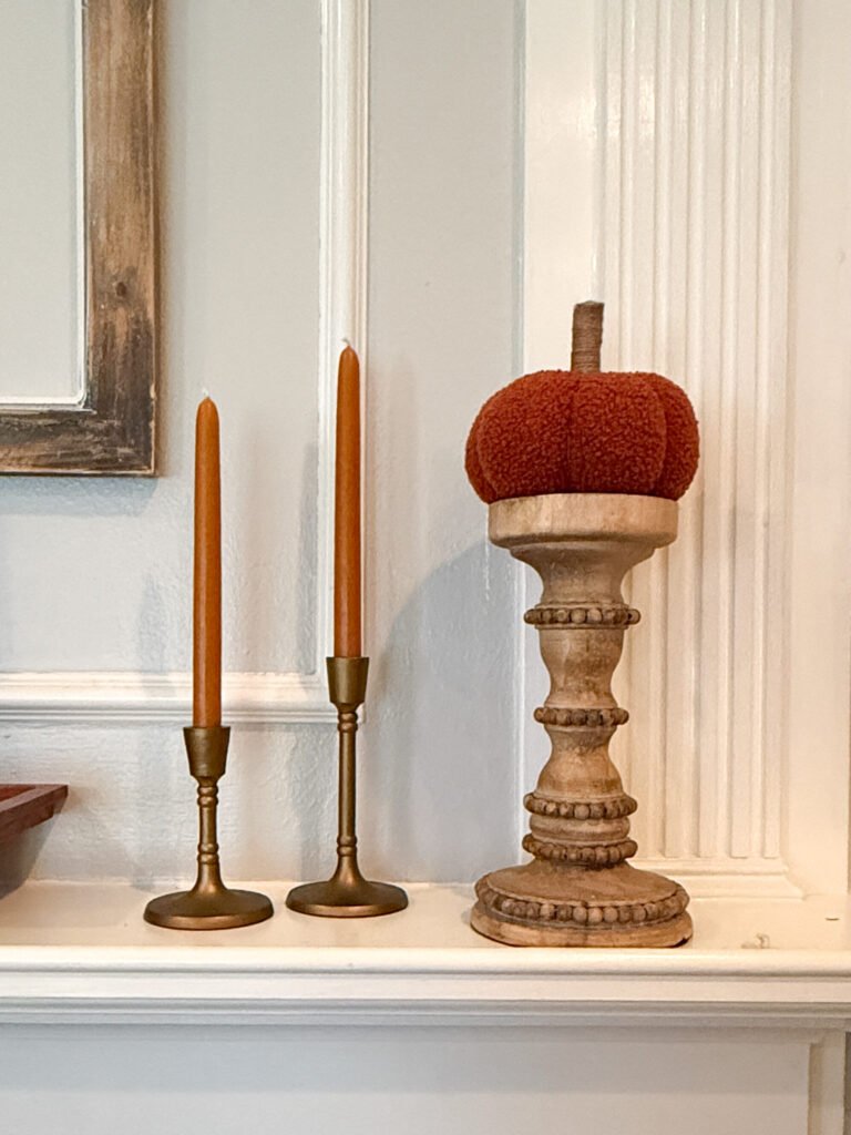 Orange pumpkin on wooden candlestick with gold candlestick holders and orange candlesticks.