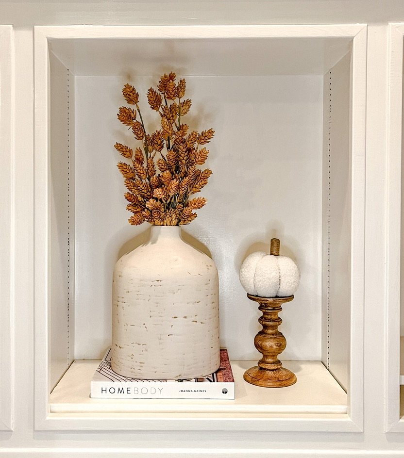Stone-textured vase with golden yellow faux florals on a shelf with a cream pumpkin and book