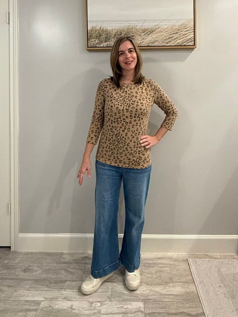 Women wearing 3/4 sleeve neutral leopard top, wide leg jeans and white sneakers.