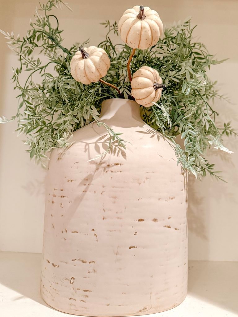 Stone-textured vase with greenery florals on a shelf with neutral white pumpkin picks. 