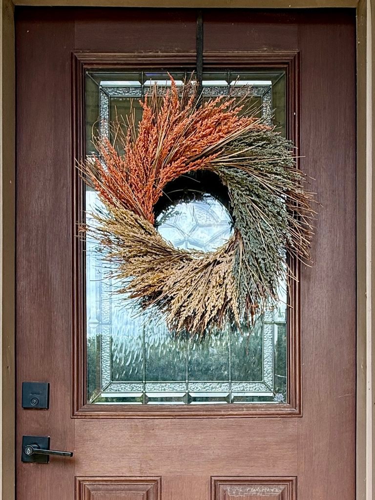 Fall wreath with cream, muted orange, and golden colored tones on front door with black metal door wreath hanger. 