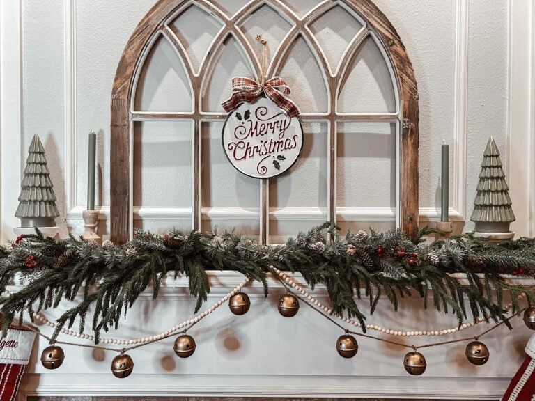 cozy Christmas mantel with gold bell garland, greenery, and wooden arch
